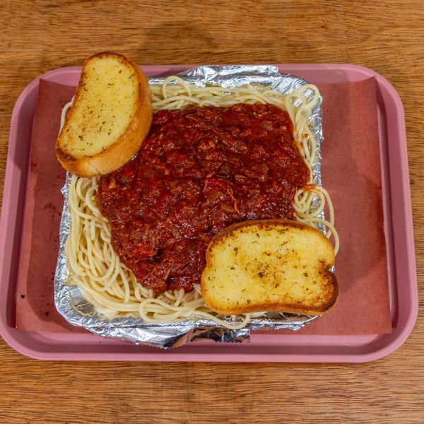 Spaghetti with red sauce and two slices of garlic bread on a pink tray.