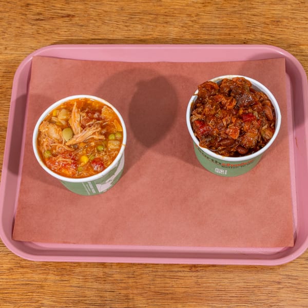 Two cups of B&B BBQ chili and Brunswick stew on a pink tray with brown paper.