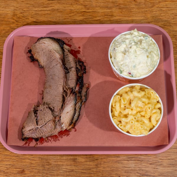Slices of B&B BBQ brisket with sides of mac and cheese and potato salad on a pink tray.