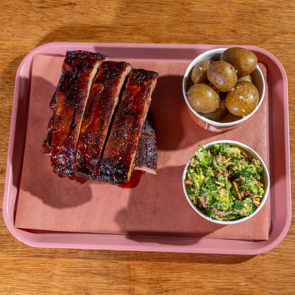 B&B BBQ ribs with a side of baby potatoes and broccoli salad on a pink tray.