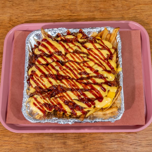 BBQ loaded fries with cheese sauce and barbecue drizzle in a foil container on a pink tray.